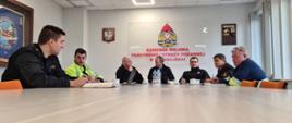 Na zdjęciu widać 7 osób siedzących przy stole na sali konferencyjnej w Komendzie Miejskiej PSP w Świnoujściu. Od lewej Kierownik Sekcji ds. kontrolno-rozpoznawczych, pracownik Gaz-System, Komendant Miejski, pracownik cywilny, Zastępca Komendanta Miejskiego, Dowódca JRG 2, pracownik Gaz-System. W tle ściana, po lewej stronie w gablocie sztandar KM PSP w Świnoujściu, następnie godło RP, logo PSP wraz z napisem pod logiem KOMENDA MIEJSKA PSP w Świnoujściu, Toporek strażacki z grawertonem.