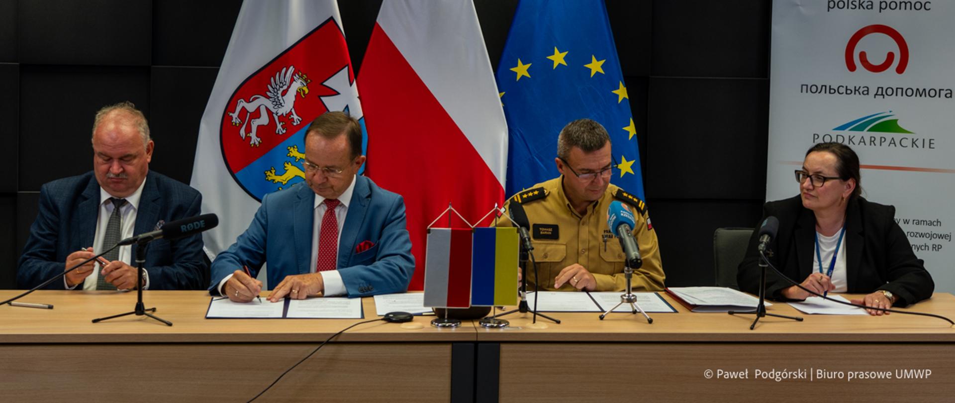 Zdjęcie zrobione wewnątrz sali konferencyjnej podczas podpisania dokumentów. Przy stole konferencyjnym siedzą sygnatariusze, wśród nich oficer Państwowej Straży Pożarnej