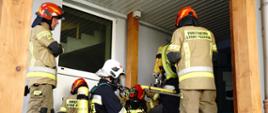 Na zdjęciu widoczni strażacy w ubraniach specjalnych koloru piaskowego w hełmach strażackich oraz sprzęt pożarniczy podczas ćwiczeń na szpitalu w Gorlicach.