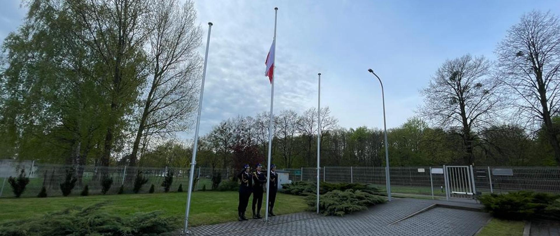 Poczet flagowy składający się z trzech umundurowanych galowo strażaków wciąga flagę państwową na maszt.