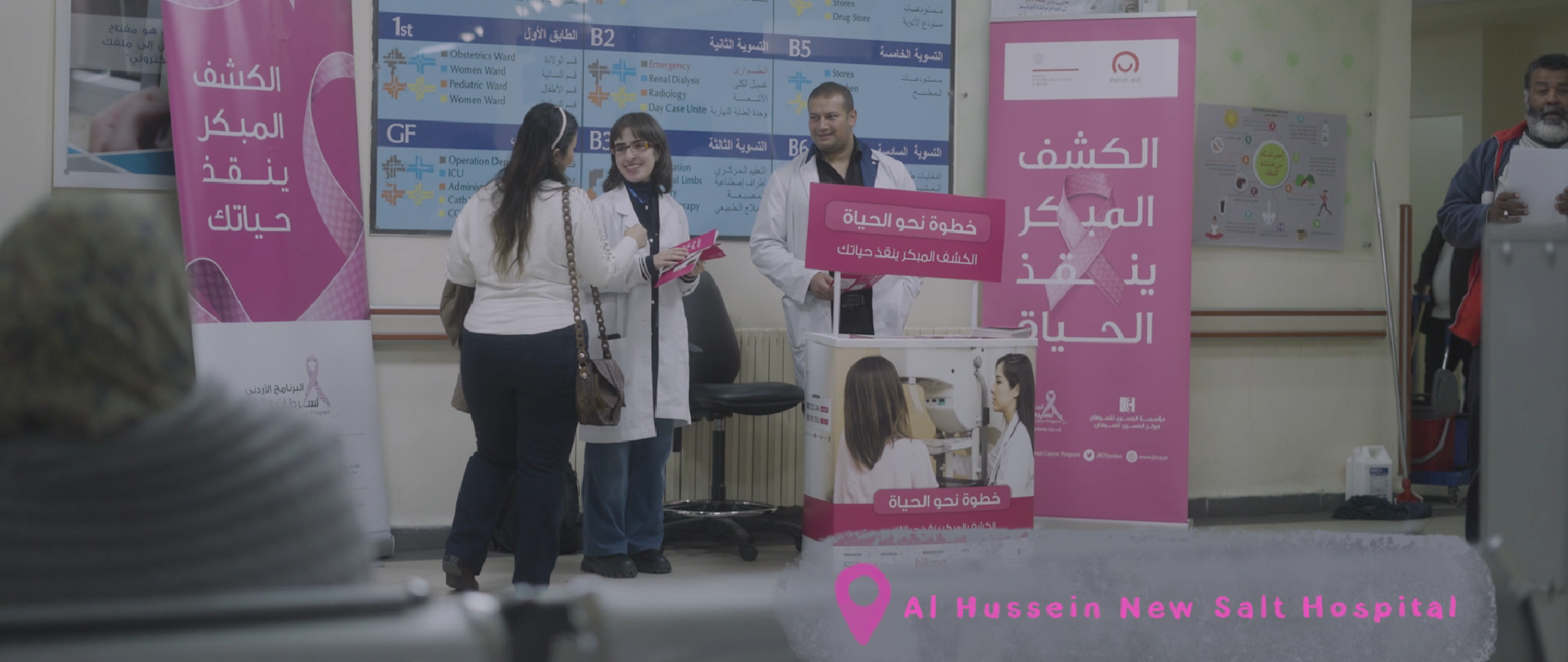 Several individuals gathered around a pink banner in a hospital lobby.