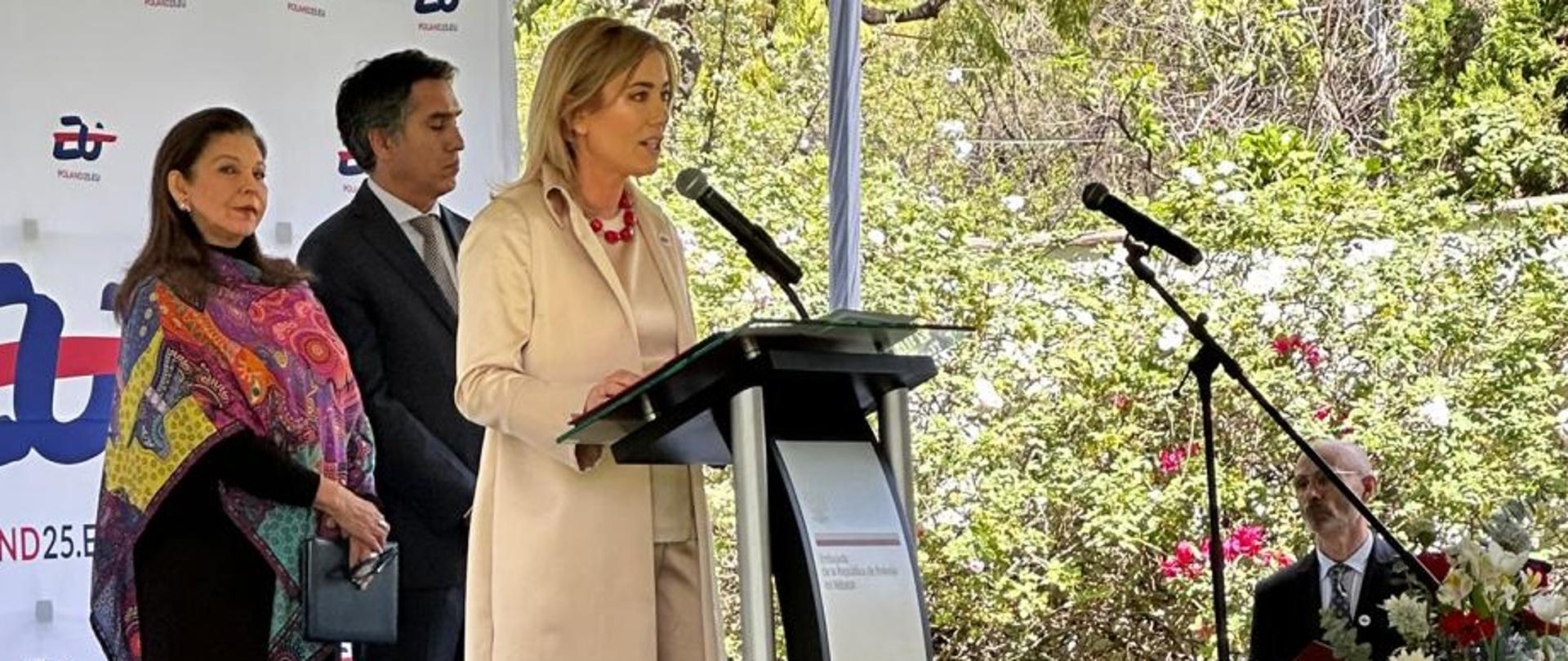 En la foto se ve a la Embajadora de Polonia en México, Agnieszka Frydrychowicz-Tekieli, de pie al aire libre junto al atril. Al fondo, el embajador de la UE en México y la subsecretaria Teresa Mercado.