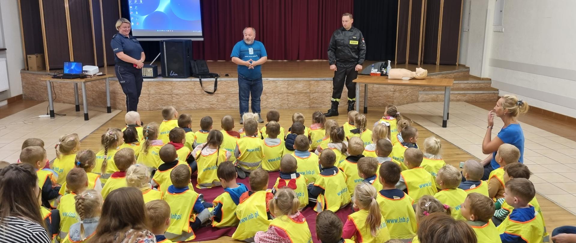Na sali siedzą dzieci prelekcje wygłaszają strażak, policjantka oraz dyrektor GOK Ryjewo