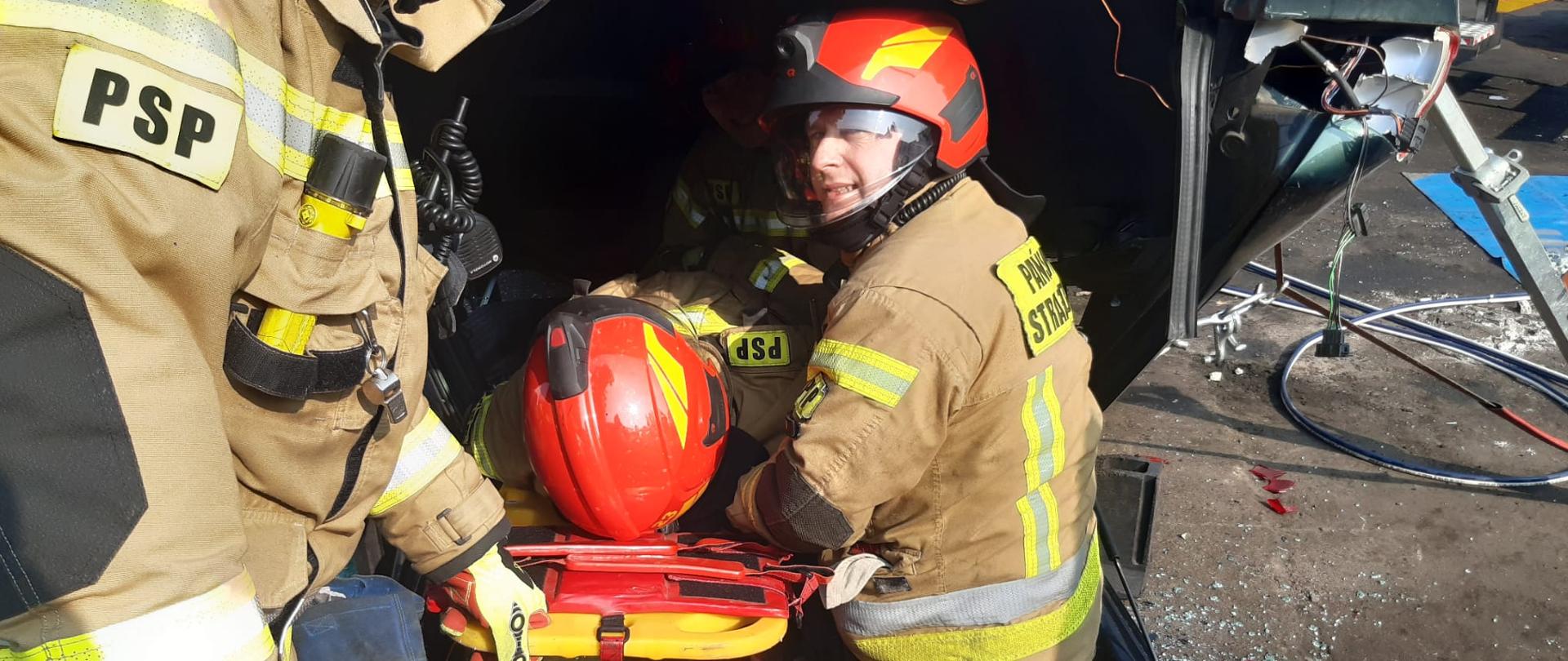 Na zdjęciu strażacy którzy ćwiczą wyciąganie osoby poszkodowanej z pojazdu.