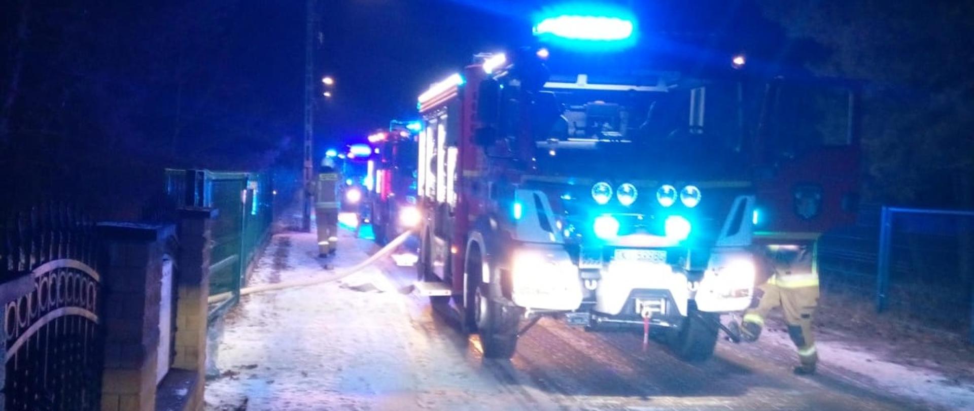 Zdjęcie przedstawia ulicę, przy której w kotłowni budynku jednorodzinnym doszło do pożaru. Na jezdni stoją samochody gaśnicze. 