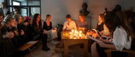zdjęcie przedstawia uczniów zgromadzonych przy stoliku na którym stoją świece i recytujących wiersze o tematyce zaduszkowej