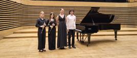 Trzy dziewczyny i jeden chłopak stoją na scenie przy fortepianie, dwie z nich trzymają klarnety.