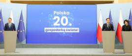 Minister Finansów i Gospodarki Andrzej Domański, Rzecznik rządu Minister Adam Szłapka i Podsekretarz Stanu w Ministerstwie Finansów Hanna Majszczyk podczas konferencji prasowej. W tle ekran "Polska 20. gospodarką świata!" oraz flagi Polski i UE.