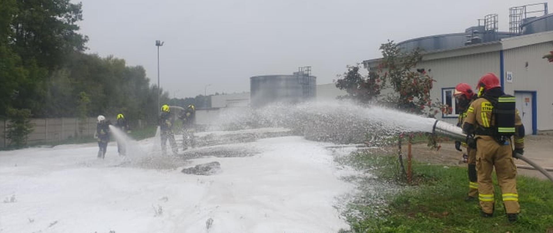 Zdjęcie przedstawia strażaków podających pianę ciężką na palącą się piankę.