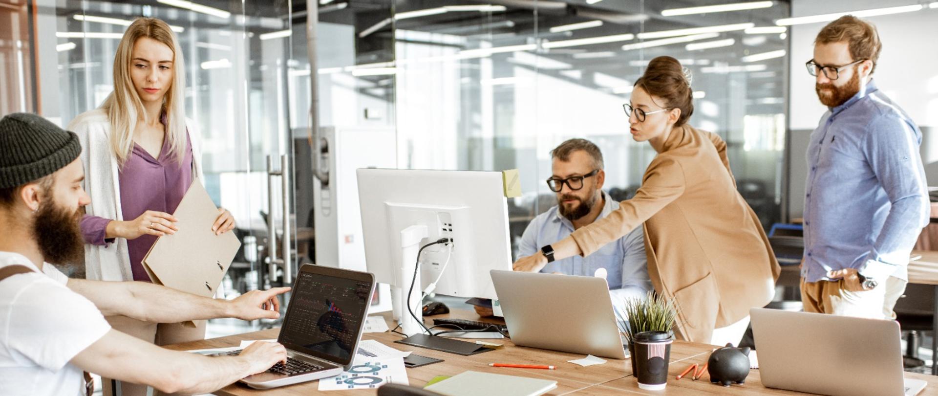 Prosta Spółka Akcyjna (P.S.A.) obchodzi dzisiaj swoje pierwsze urodziny. Na zdjęciu widać pracujących przy biurkach, przed komputerem ludzi w biurze. 