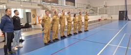 Strażacy stoją na sali sportowej podczas rozpoczęcia turnieju 