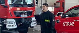 Nowy strażak w ubraniu koszarowym na tle samochodów tutejszej jednostki podczas ślubowania