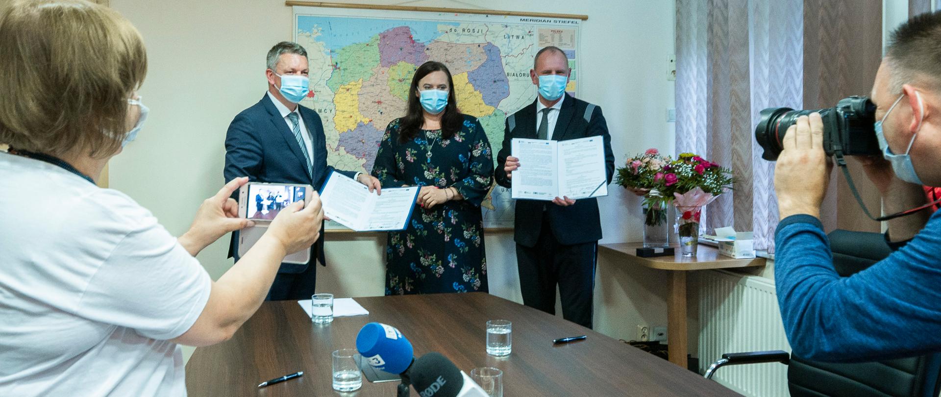 uczestnicy spotkania prezentują podpisaną umowę grantową, obecni na sali dziennikarze fotografują uczestników