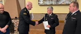 Komendant Powiatowy Państwowej Straży Pożarnej w Działdowie, składa gratulacje naczelnikowi OSP Rumian i uściska dłoń. Obok stoją Wójt Gminy Rybno i prezes OSP Rumian. 