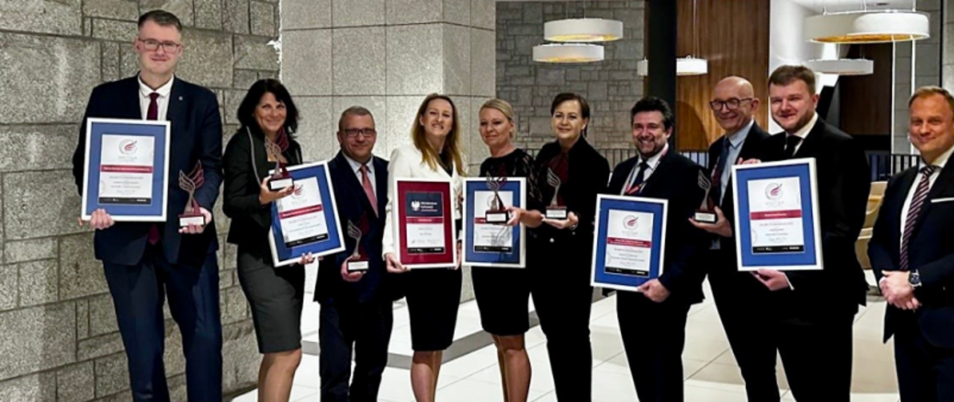 Dorota Cabańska, Główny Inspektor Nadzoru Budowlanego, wraz z innymi laureatami nagrody Skrzydła IT w Administracji, trzymający statuetki i dyplomy podczas uroczystej gali w eleganckim wnętrzu.