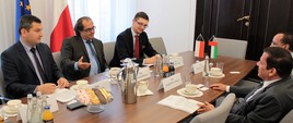 Minister Marek Gróbarczyk i Ambasador ZEA rozmawiają siedząc przy stole. Ministrowi towarzyszy dwóch przedstawicieli ministerstwa, Ambasadorowi jego współpracownik.