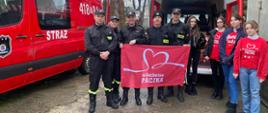 Strażacy na czele komendantem powiatowym PSP w Jędrzejowie mł. bryg. Mariuszem Stolarczykiem oraz wolontariuszami „Szlachetnej paczki”. Wszyscy trzymają czerwoną flagę akcji charytatywnej „Szlachetna paczka”.