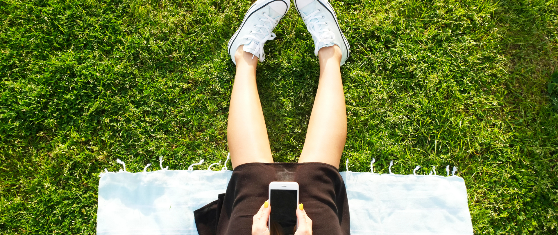 Kobieta z telefonem siedząca na trawie.