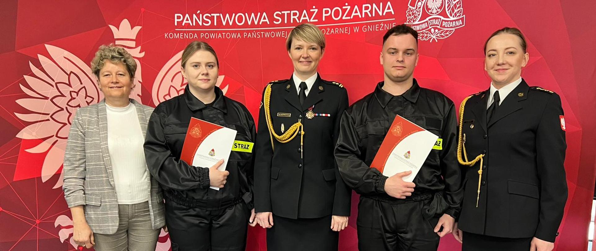 Na zdjęciu widać pięć osób (cztery kobiety i jeden mężczyzna) na czerwonym tle. 