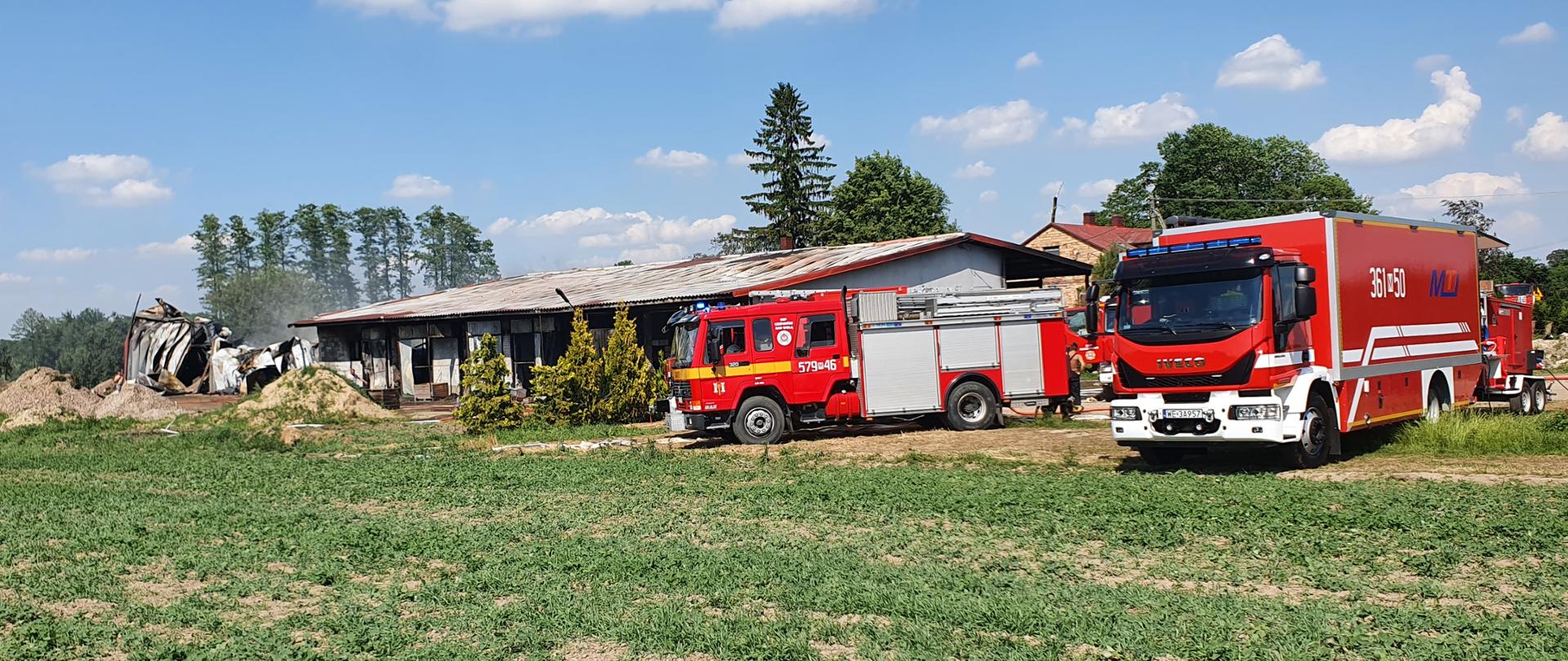 Pożar w Garwolewie, strażacy gaszący pożar budynku przechowalni. Na pierwszym planie samochody gaśnicze koloru czerwonego