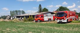 Pożar w Garwolewie, strażacy gaszący pożar budynku przechowalni. Na pierwszym planie samochody gaśnicze koloru czerwonego