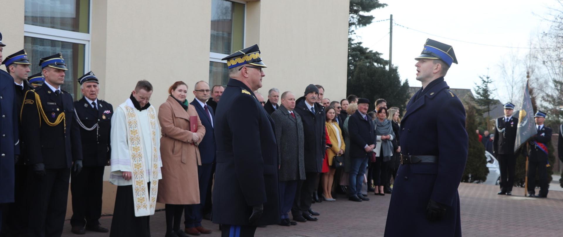 Zdjęcie przedstawia uroczysty apel przekazania samochodu ratowniczo-gaśniczego. Na pierwszym planie Kujawsko-Pomorski Komendant Wojewódzki Państwowej Straży Pożarnej oraz dowódca uroczystości składający meldunek otwarcia uroczystości. NA drugim planie zaproszeni goście wraz z przedstawicielami administracji rządowej.