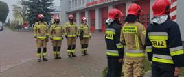 Siedmiu strażaków podczas podnoszenia flagi państwowej przed budynkiem Komendy Straży