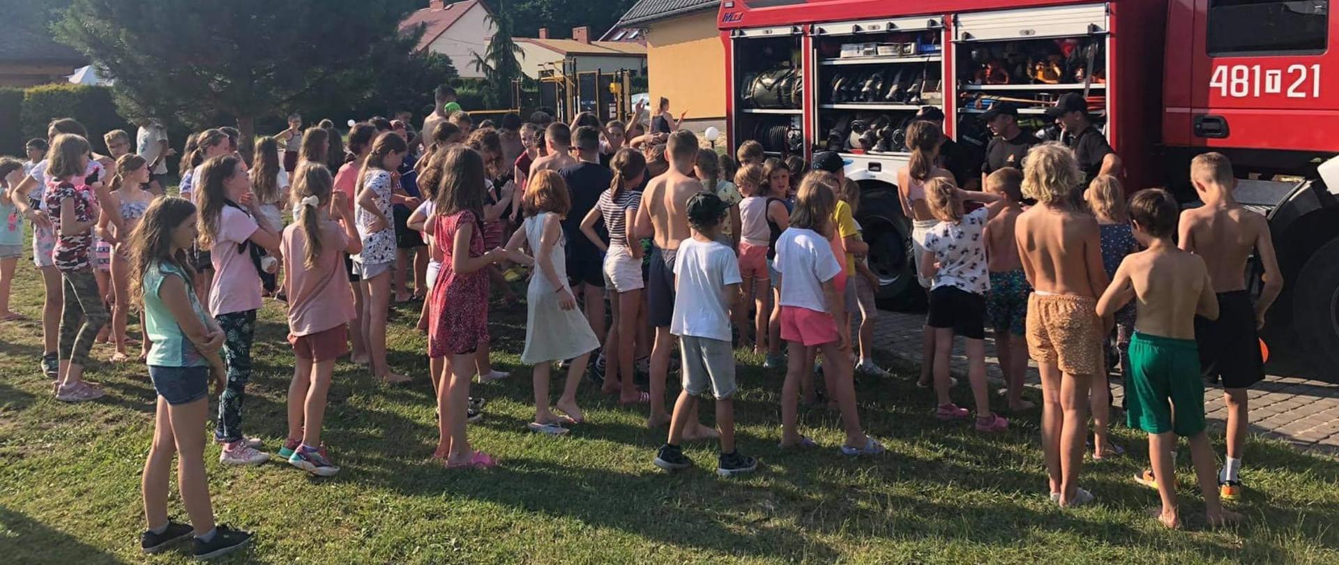 Na zdjęciu widzimy jak skarżyscy strażacy prezentują dzieciom wypoczywających na terenie Hotelu PARADISO sprzęt ratowniczo-gaśniczy znajdujący się na wyposażeniu samochodu pożarniczego.