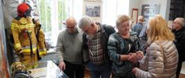 Na zdjęciu podczas wernisażu wystawy „Na STRAŻY bezpieczeństwa mieszkańców Ziemi Gorlickiej" widoczni w ubraniach cywilnych zaproszeni na wernisaż goście 6 osób oglądający wystawę. W tle widoczne zdjęcia i eksponaty pożarnicze pompy, działko, węże pożarnicze, hełmy, radiostacje, ubranie strażackie specjalne koloru pisakowego. 