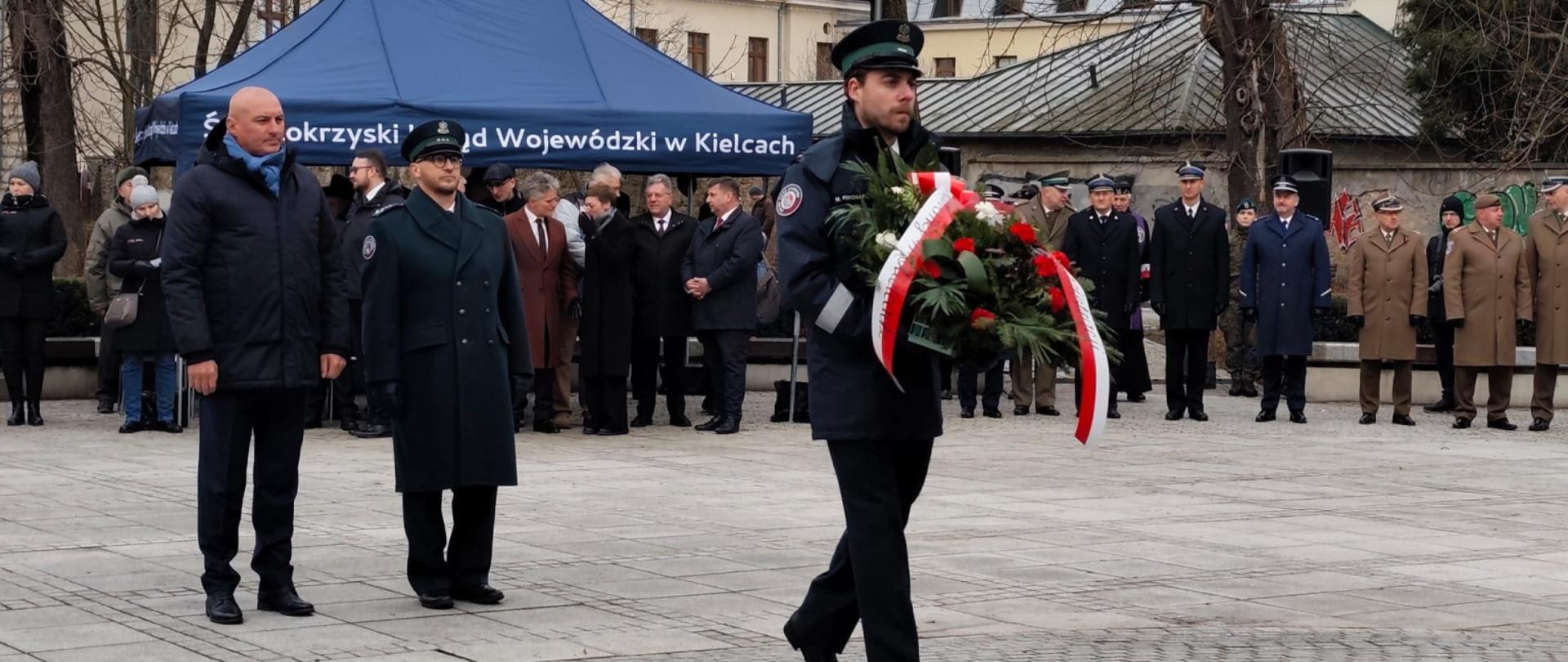 Funkcjonariusz niesie wieniec pod pomnik AK