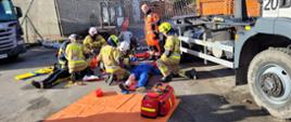 Zdjęcie przedstawia strażaków udzielających pomocy medycznej osobom poszkodowanym podczas ćwiczeń. 