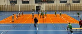 Zdjęcie przedstawia strażaków grających w piłkę siatkową na hali sportowej. 