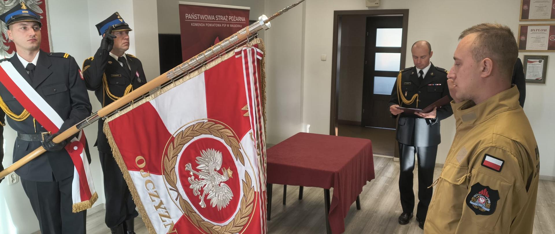Strażak podczas ślubowania stoi przed pocztem sztandarowym