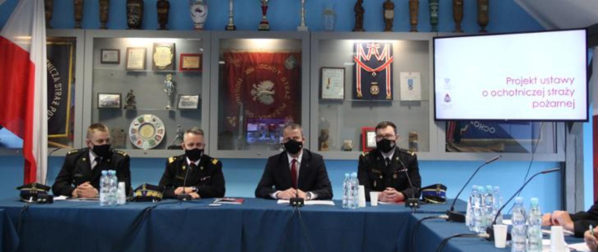 Na zdjęciu widać czterech strażaków za stołem prezydialnym w trakcie spotkania