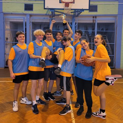 zdjęcie przedstawia drużynę w niebieskich koszulkach z pucharem zwycięstwa we wspólnym zdjęciu pod koszem na sali gimnastycznej