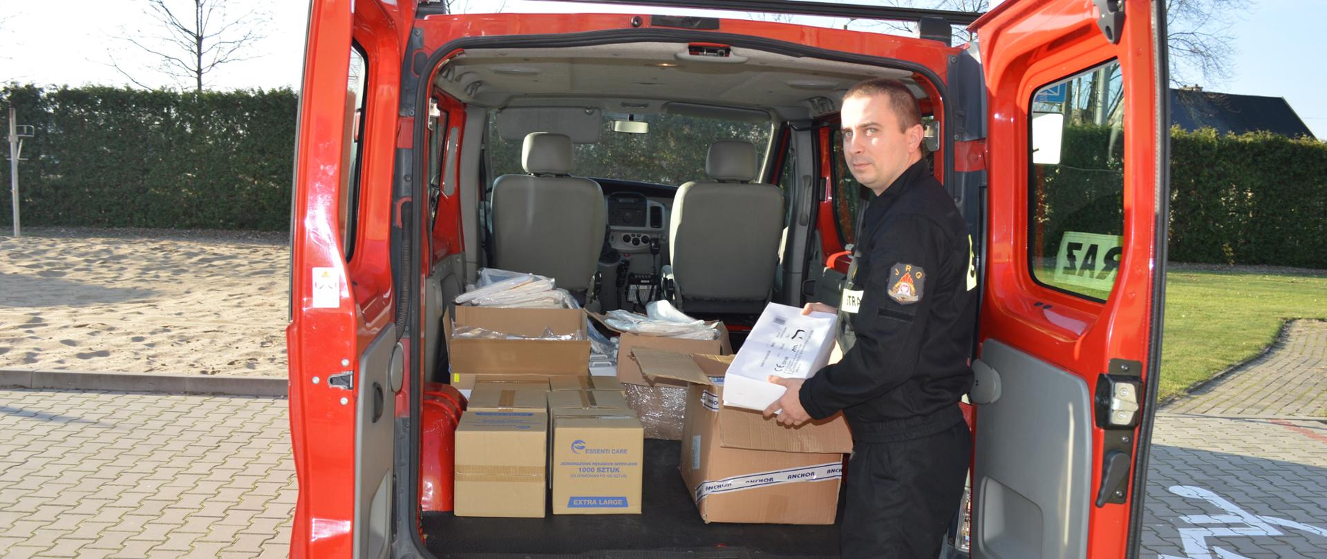 Na zdjęciu środki ochrony osobistej w samochodzie przy którym stoi strażak PSP