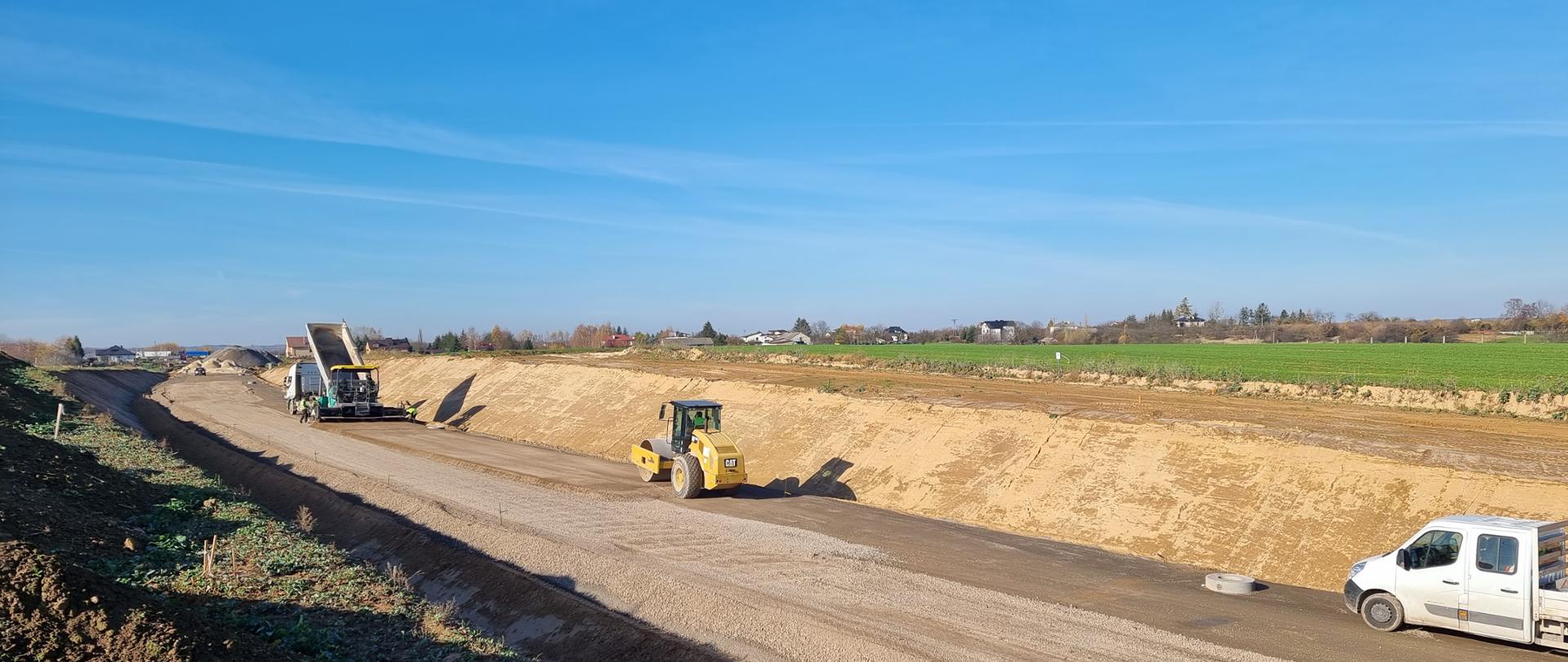 DK9 budowa obwodnicy Ostrowca Świętokrzyskiego - wykonywanie podbudowy z kruszywa i warstwy mrozoochronnej, ślad drogi wykopie, walec, rozściełacz, samochód dostawczy 