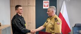 Komendant Powiatowy Państwowej Straży Pożarnej w Człuchowie st. bryg. Radosław Batruch stoi w gabinecie i wręcza akt mianowania na stanowisko dowódcy zmiany st. asp. Karolowi Płóciennik.