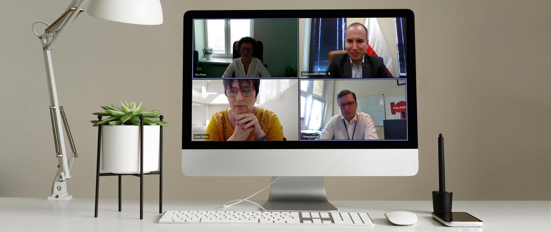 Stojące na biurku komputer, na jego ekranie, w czterech oknach, widoczni uczestnicy spotkanie, w tym minister Adam Andruszkiewicz.