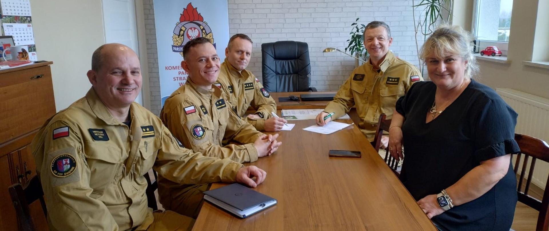 Zdjęcie przedstawia spotkanie w KP PSP Świdwin kadry kierowniczej z koordynatorem Centrum Zdrowia Psychicznego MSWiA w Świdwinie . Uczestnicy siedzą przy stole i rozmawiaja.