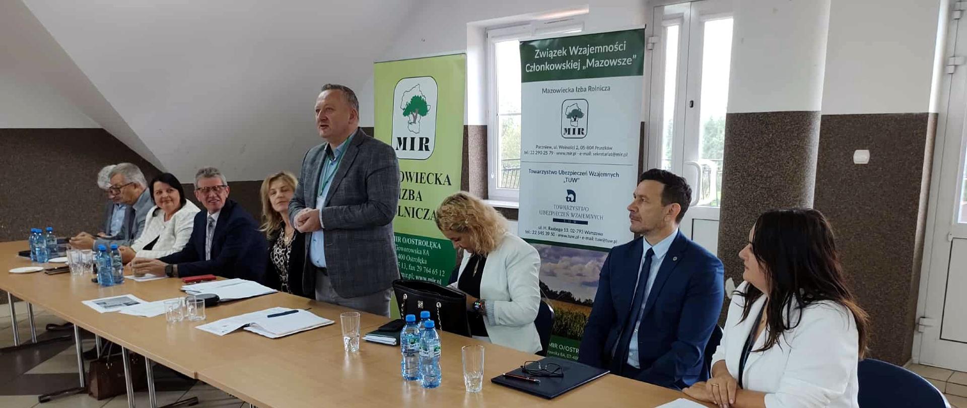 Panel dyskusyjny z udziałem przedstawicieli Mazowieckiej Izby Rolniczej – przy długim stole siedzi kilka osób w garniturach i eleganckich strojach, a jeden z mężczyzn wstaje i przemawia; w tle widoczne są banery organizacji rolniczych.