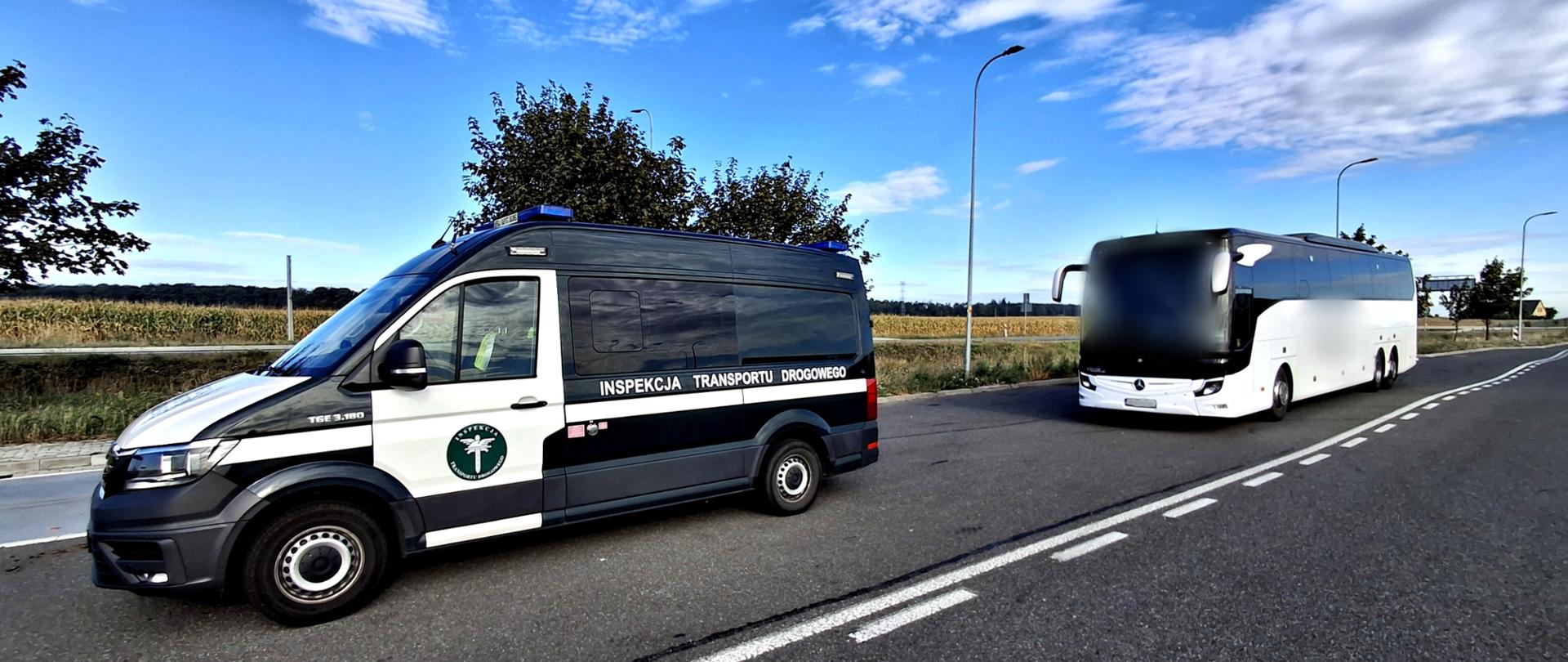 Oznakowany samochód Inspekcji Transportu Drogowego stojący przy drodze, a kilka metrów za nim biały autokar. W tle widoczne są pola, drzewa i latarnie uliczne.