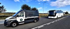 Oznakowany samochód Inspekcji Transportu Drogowego stojący przy drodze, a kilka metrów za nim biały autokar. W tle widoczne są pola, drzewa i latarnie uliczne.