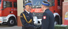 Zmiany kadrowe w rawickiej komendzie. Zmiany kadrowe w rawickiej komendzie. Plac przed komendą powiatową, na którym odbywa się uroczysty apel. Na tle samochodów pożarniczych komendant powiatowy składa podziękowania strażakowi, który zdał obowiązki dowódcy JRG.