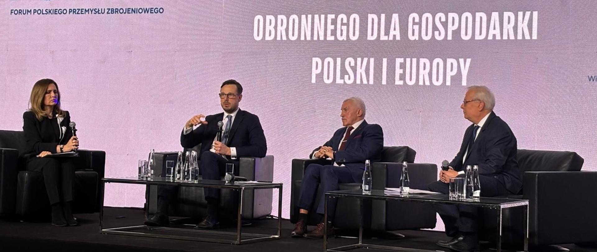 Minister Jakub Jaworowski wraz z innymi panelistami siedzą na scenie. W tle ekran z napisem: Znaczenie polskiego przemysłu obronnego dla gospodarki Polski i Europy.