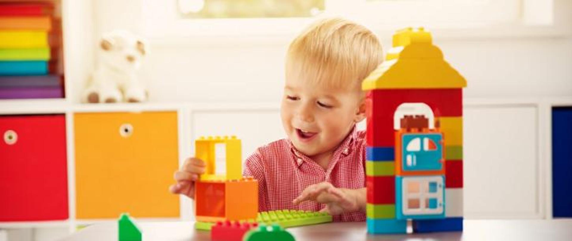 uśmiechnięty chłopiec około 4-5 lat bawiący się kolorowymi klockami.