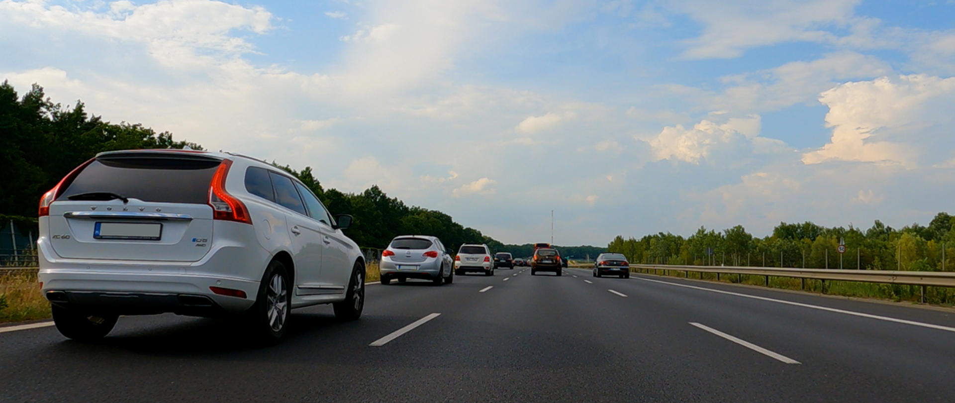 Samochody na drodze szybkiego ruchu, trzy pasu ruchu, po obu stronach drogi las, zdjęcie zrobione z tyłu pojazdów