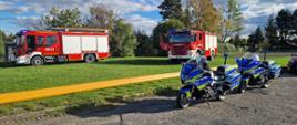 Na zdjęciu znajdują się 2 samochody strażackie oraz dwa motocykle policyjne w tle widać drzewa