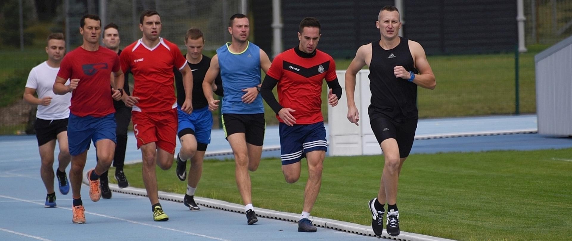na zdjęciu ośmiu biegaczy w trakcie biegu po niebieskiej bieżni