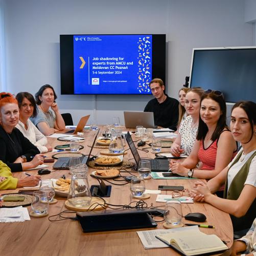 W sali szkoleniowej przy stole konferencyjnym 11 osób z laptopami oraz ciasteczkami. Z tyłu wyświetlana jest prezentacja Job shadowing for experts from AMCU and Moldovan CC Poznań z logo Polska pomoc